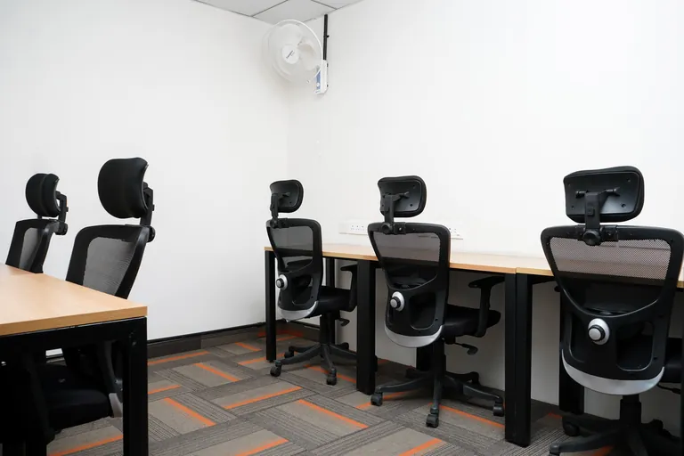 Private cabin with wall-side desks and office chairs at Suits Vaishali Nagar